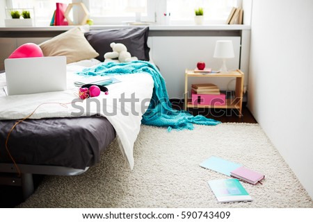 Stylish teen girl messy bedroom with blanket hanging down from bed and books lying on white soft carpet