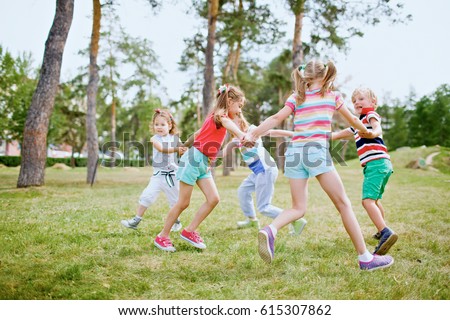 Group of children holding hands and dancing in circle on green lawn in park on beautiful summer day