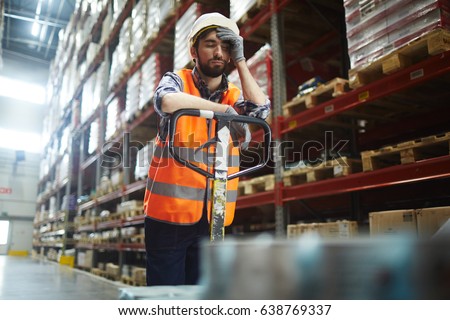 Tired worker with forklift touching his forehead