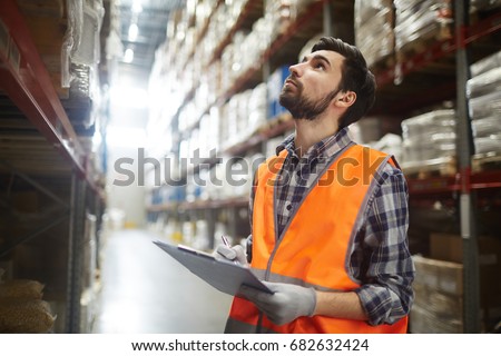 Portrait of warehouse worker looking up the tall shelves doing inventory control