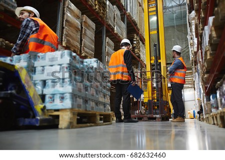 Group of several loaders working in warehouse aisle between tall racks, moving pallets with packed goods
