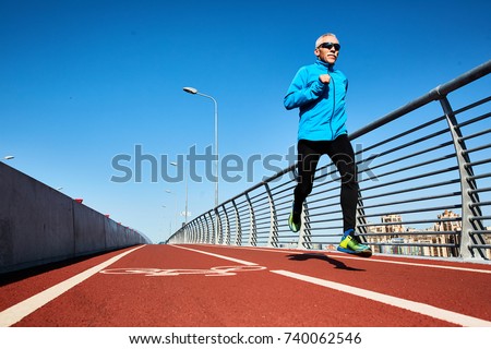 Low angle view of concentrated senior sportsman jogging outdoors and enjoying sunny warm day, full length portrait