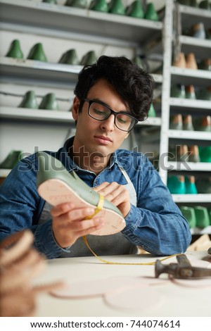 Young shoe designer measuring form of boot in process of work