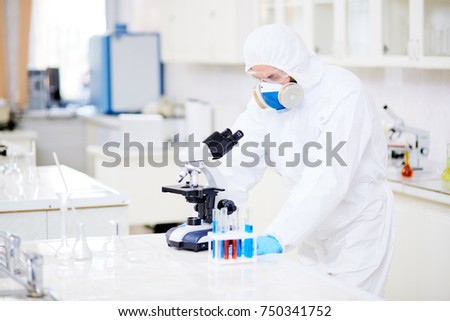 Modern clinician studying new virus in microscope in chemical laboratory