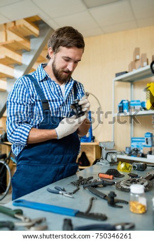 Gloved repairman looking at spare part by his workplace