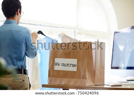 Rear view of clothes designer and paperbag with new collection sticker on his workplace
