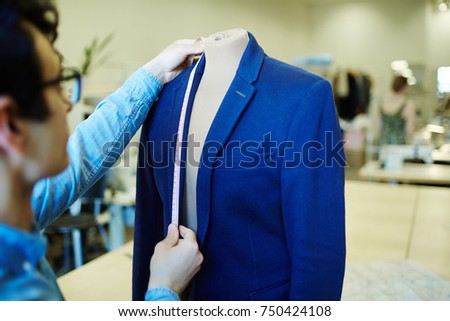 Self-employed tailor taking measures from jacket on dummy in his workshop