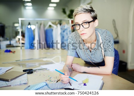 Businesswoman with blue crayon sketching by workplace in her fashion-studio or boutique