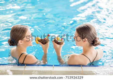 Friendly girls toasting with coconut drinks in swimming-pool at spa resort