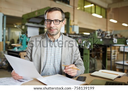 Successful engineer with paper looking through technical documents in workshop