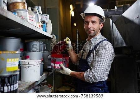 Modern factory worker holding container with red paint in storehouse