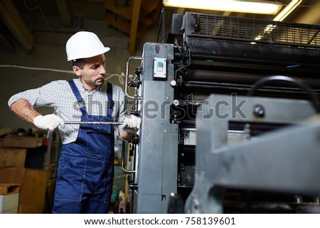 Contemporary engineer or technician in gloves, harhat and uniform doing his work