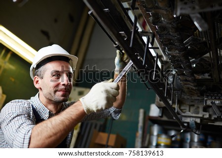 Contemporary industrial repairman fixing detail of huge machine