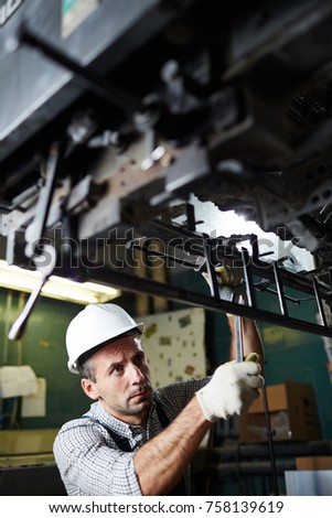 Technician with spanner adjusting parts of modern industrial equipment