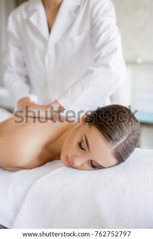 Relaxed girl having massage of her back in day spa salon by professional masseuse