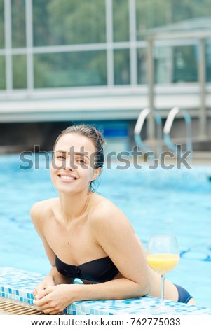 Cheerful young female in swimming-pool looking at camera with smile