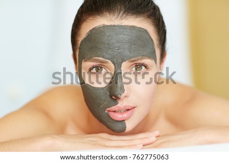 Young woman with clay mask on half of her face looking at camera