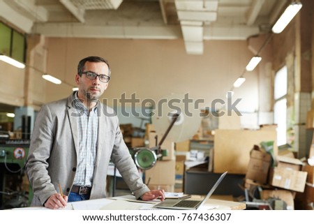 Modern factory worker with laptop searching for online data by workplace