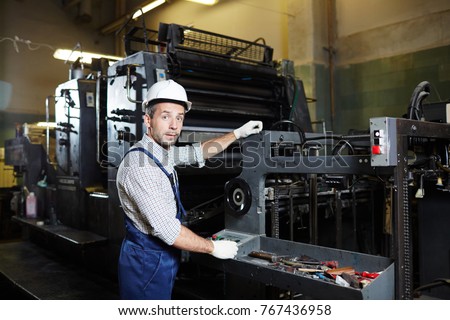 Modern factory technician in uniform starting industrial machine and checking its operability