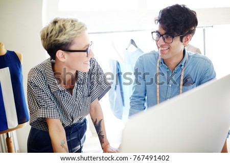Two young tailors discussing new fashion trends during work