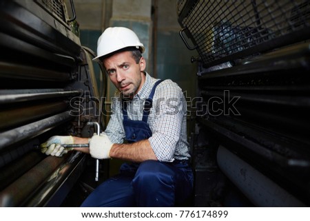 Serious factory worker sitting by industrial machine and repairing its start system