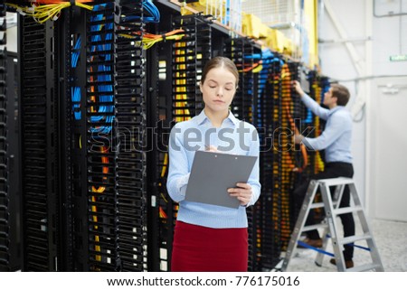 Young woman making notes during technical experiment or testing new bitcoin storage equipment