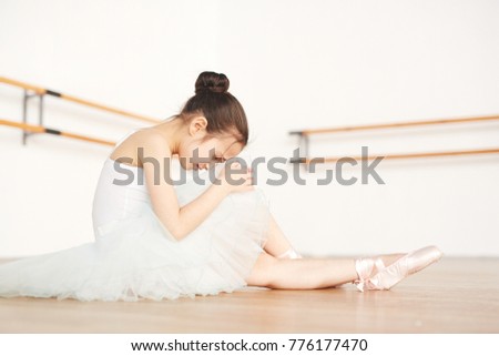 Cute girl in ballerina outfit sitting on the floor of classroom and crying because of dancing troubles