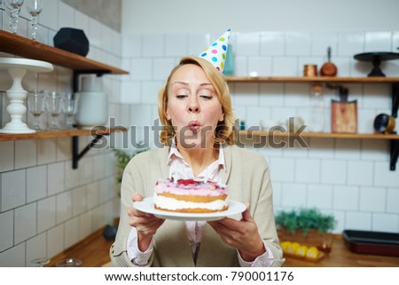 Mid-aged woman blowing burning candles on birthday cake in the kitchen