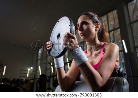 Strong active female with barbell plate lifting it during training in gym