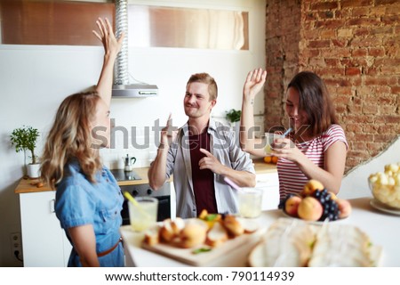 Young dancing friends with drinks having home party in the kitchen