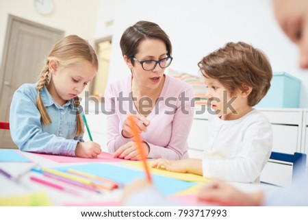 Kindergarten teacher showing and explaining kids how to draw objects