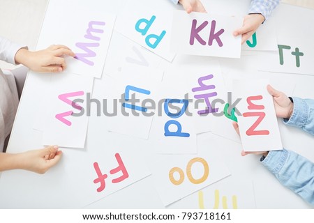 Hands of kids holding paper cards with colorful letters during alphabet play