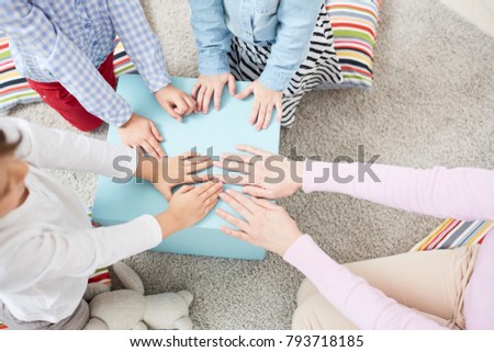 Young woman and three kids putting hands on cover of big box while playing on the floor