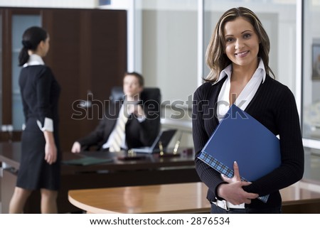 Pretty businesswoman holding the document case in the office with two another persons on the background