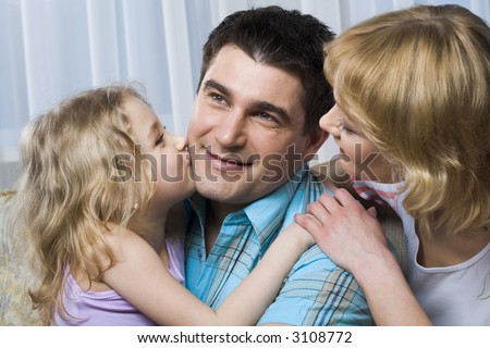 Angel like daughter kissing her happy father and her loving mother is hugging him at the moment