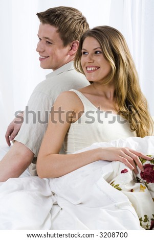 Young laughing couple sitting back to back on the bad