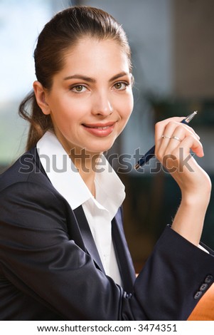Elegant brunette woman in dark gray suit with a pen in her hand gazing at the camera