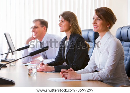 Successful young woman speaking in public on microphone sitting at the table in black comfortable chairs among her colleagues