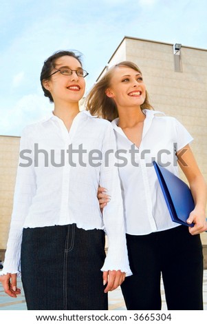 Two businesswomen looking upwards holding blue document case standing outside the office building