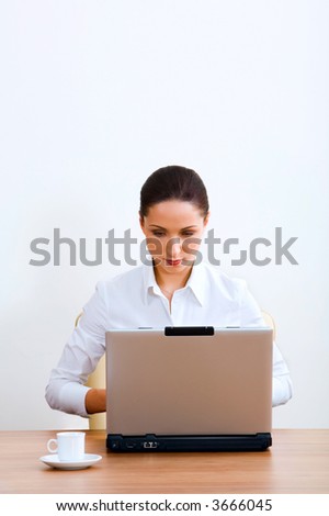 Isolated on white portrait of serious brunette businesswoman working on the laptop sitting at the table with a white cup on it