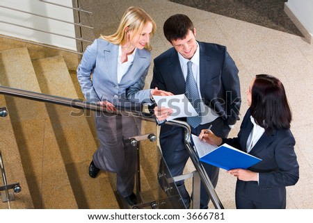 Three businesspeople run across on the stairs of the business building showing documents to each other and making notes