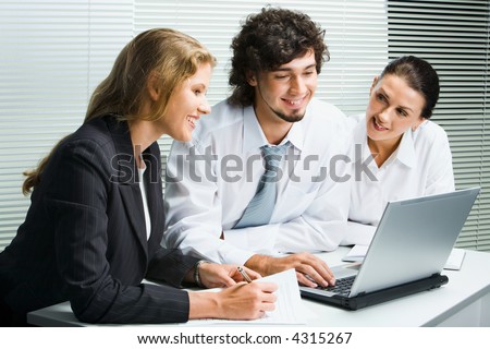 Group of three young business people gathered together around the laptop discussing an interesting idea