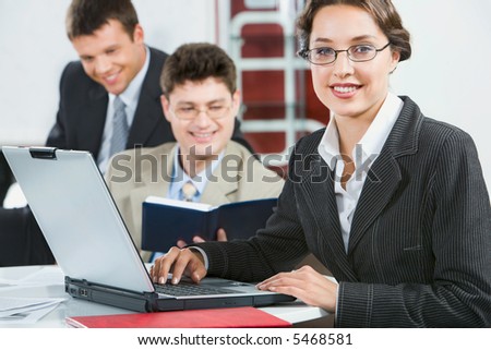 Young attractive consultant is sitting at the table on the background of her colleagues