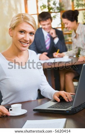 Confident business woman in white blouse sitting at the table with cup, laptop, paper on it