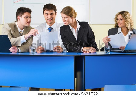 Group of people sitting at the blue table and discussing business questions in the room