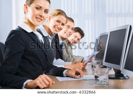 Portrait of confident people sitting in a line in front of monitors and looking at camera
