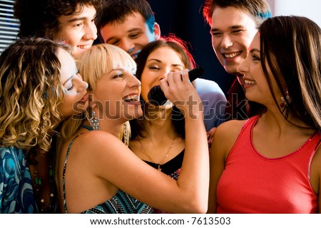 Pretty woman sings a song in the environment of her friends at a karaoke party