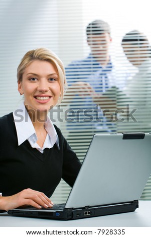 Young successful smiling woman sitting at the table and typing on the laptop
