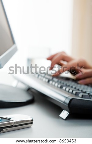 Image of human hands on the keyboard with the cellular phone lying near by