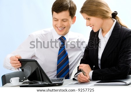 Image of two successful business people sitting at the table and looking at the screen of the laptop with smiles